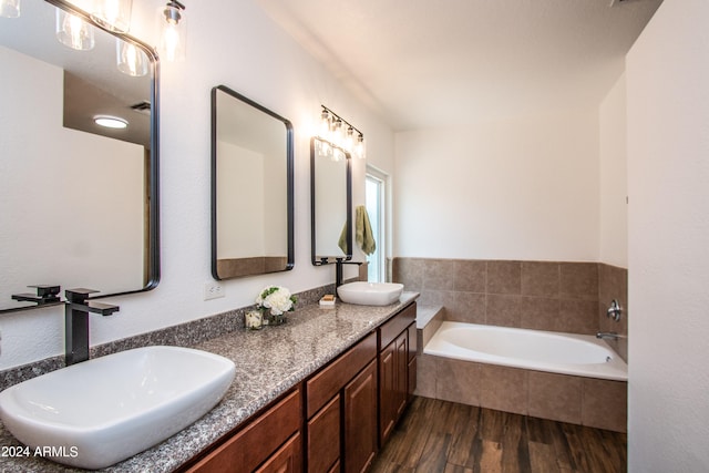 bathroom featuring wood-type flooring, tiled bath, and vanity