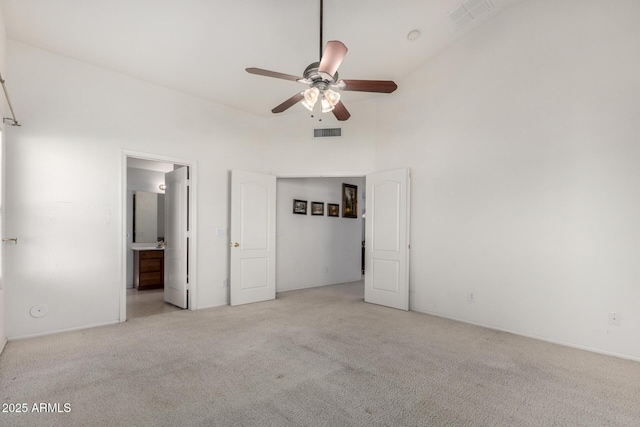 unfurnished bedroom with light colored carpet, visible vents, a towering ceiling, and connected bathroom