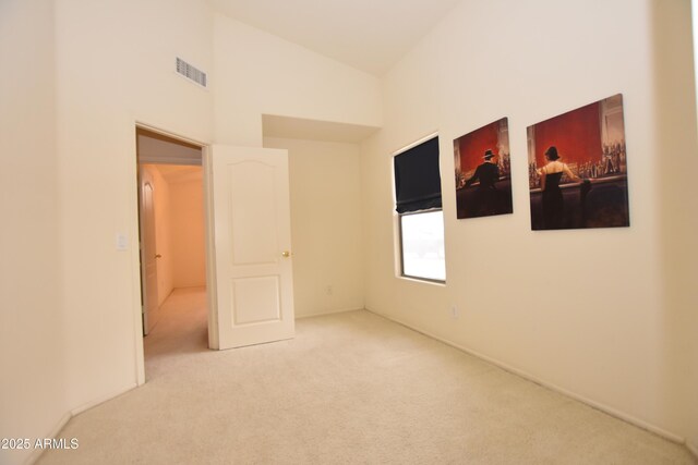 carpeted empty room featuring lofted ceiling and visible vents