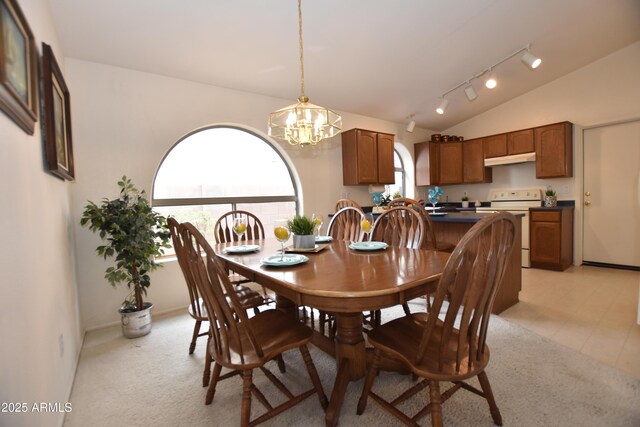 dining space with a notable chandelier, track lighting, light colored carpet, and vaulted ceiling