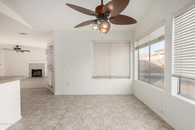 empty room with a tiled fireplace, baseboards, a ceiling fan, and light tile patterned flooring