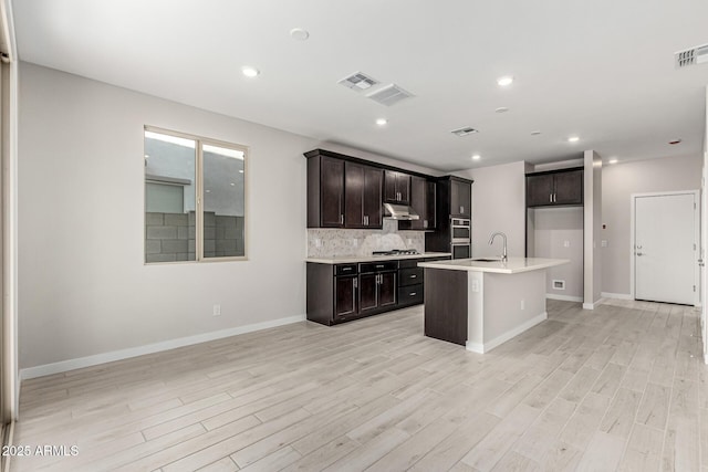 9366 E Sequence Ave, Mesa, AZ 85212 - kitchen featuring under cabinet range hood, light wood-style flooring, light countertops, tasteful backsplash, and a center island with sink