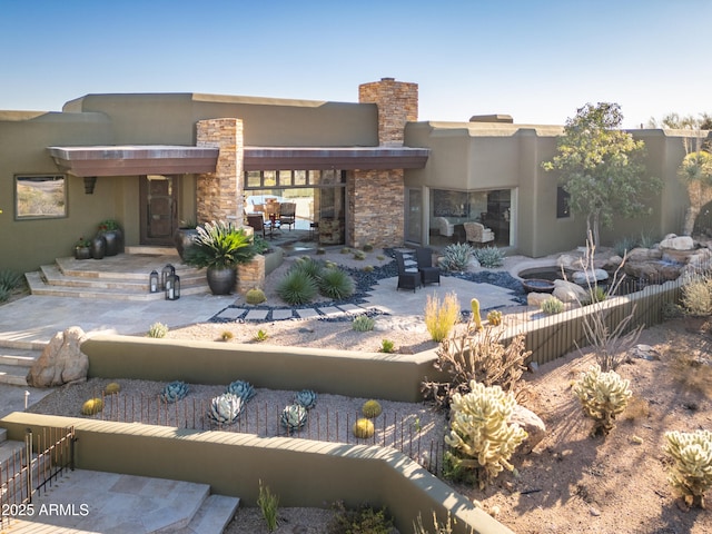 rear view of house with stone siding, a patio area, fence, and stucco siding