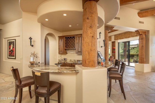 bar with beam ceiling, light stone countertops, and ornate columns