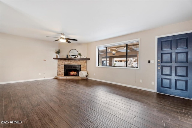 unfurnished living room with ceiling fan, a stone fireplace, and dark hardwood / wood-style flooring