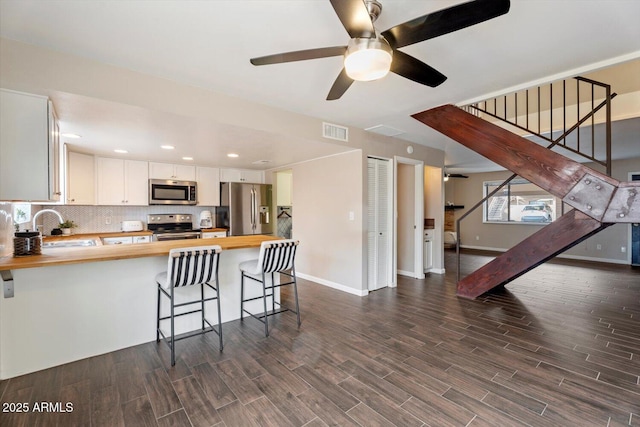 kitchen featuring wooden counters, a kitchen breakfast bar, stainless steel appliances, white cabinets, and kitchen peninsula