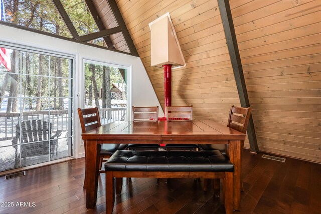 dining area featuring visible vents, wood walls, lofted ceiling, and dark wood-style flooring