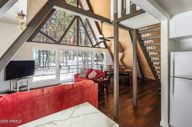 living room featuring dark wood-type flooring, beamed ceiling, plenty of natural light, and stairway