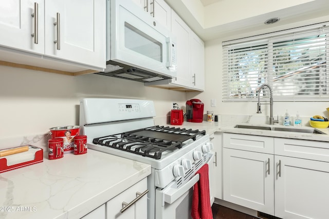 kitchen with white cabinets, white appliances, light stone countertops, and a sink