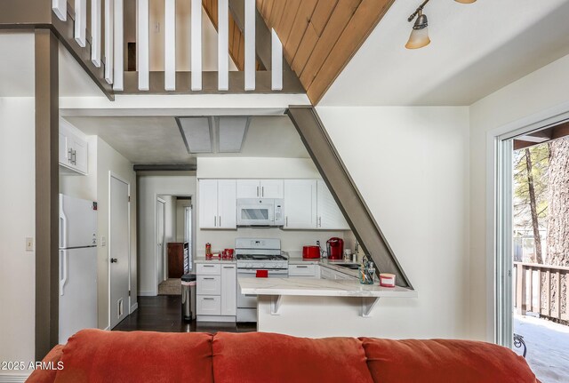 kitchen featuring light countertops, a peninsula, white cabinets, white appliances, and a sink