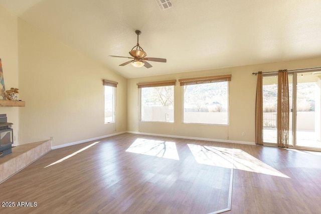 unfurnished living room featuring ceiling fan, hardwood / wood-style floors, vaulted ceiling, and a wood stove