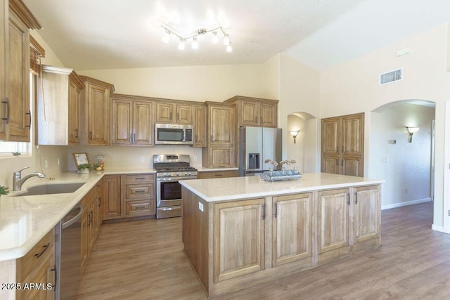 kitchen with light hardwood / wood-style floors, appliances with stainless steel finishes, sink, a kitchen island, and high vaulted ceiling