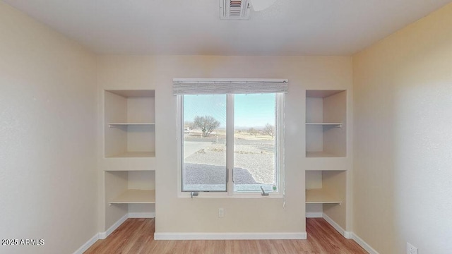 empty room with light hardwood / wood-style floors and built in shelves