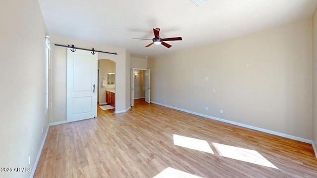 unfurnished bedroom with light wood-type flooring, ceiling fan, ensuite bathroom, and a barn door