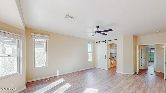 unfurnished room featuring a barn door, light hardwood / wood-style floors, and a healthy amount of sunlight