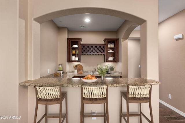 bar featuring dark wood-style floors, arched walkways, indoor wet bar, and baseboards