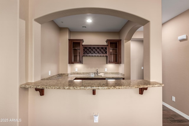 kitchen with dark wood finished floors, glass insert cabinets, a breakfast bar, a peninsula, and light stone countertops