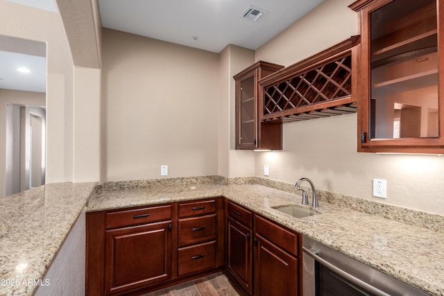 kitchen with light stone countertops, visible vents, glass insert cabinets, a sink, and wood finished floors