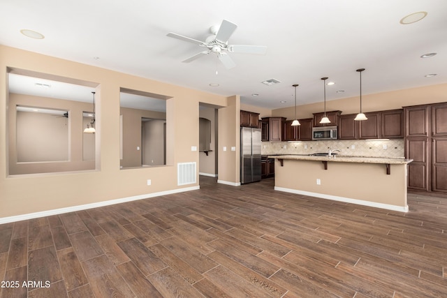 kitchen with a breakfast bar, visible vents, appliances with stainless steel finishes, decorative backsplash, and dark wood finished floors