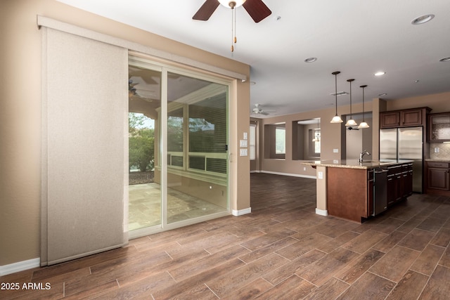 kitchen featuring a center island with sink, light stone counters, open floor plan, decorative light fixtures, and wood finish floors