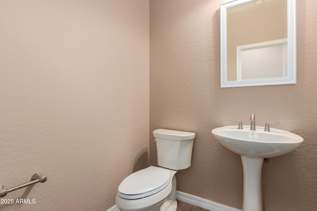 half bathroom with toilet, baseboards, a sink, and a textured wall