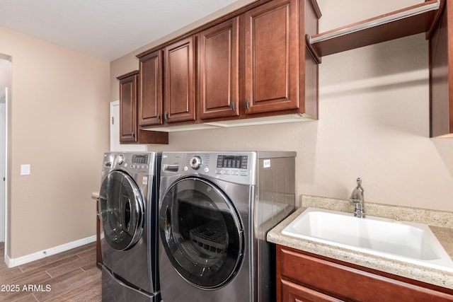 clothes washing area with washing machine and clothes dryer, cabinet space, wood tiled floor, a sink, and baseboards