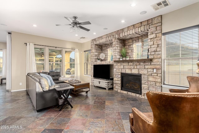 living area with visible vents, baseboards, a fireplace, stone tile flooring, and a ceiling fan