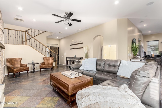 living room featuring visible vents, stairs, ceiling fan, stone tile flooring, and arched walkways