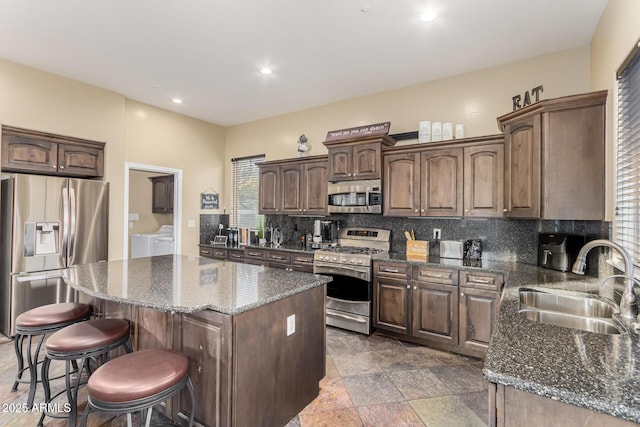 kitchen with washing machine and clothes dryer, a breakfast bar, tasteful backsplash, appliances with stainless steel finishes, and a sink
