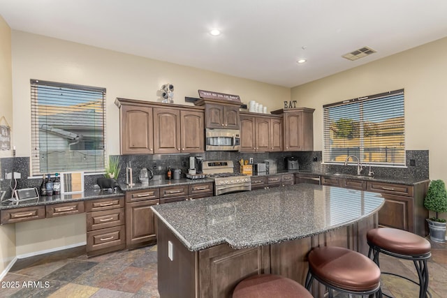 kitchen featuring a sink, backsplash, a kitchen breakfast bar, stainless steel appliances, and visible vents