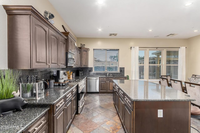 kitchen featuring visible vents, stainless steel appliances, dark brown cabinets, a kitchen island, and backsplash