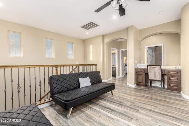 living area with light wood-style flooring, visible vents, baseboards, ceiling fan, and arched walkways