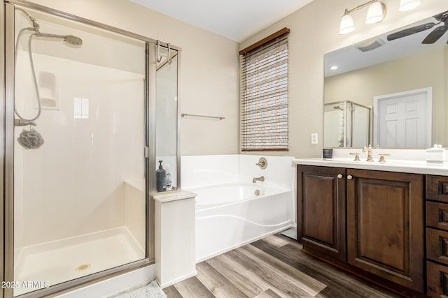 bathroom with vanity, a bath, a stall shower, a ceiling fan, and wood finished floors