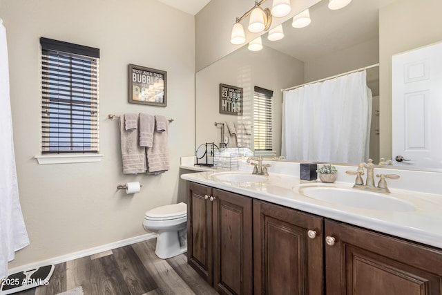 bathroom with double vanity, a sink, toilet, and wood finished floors