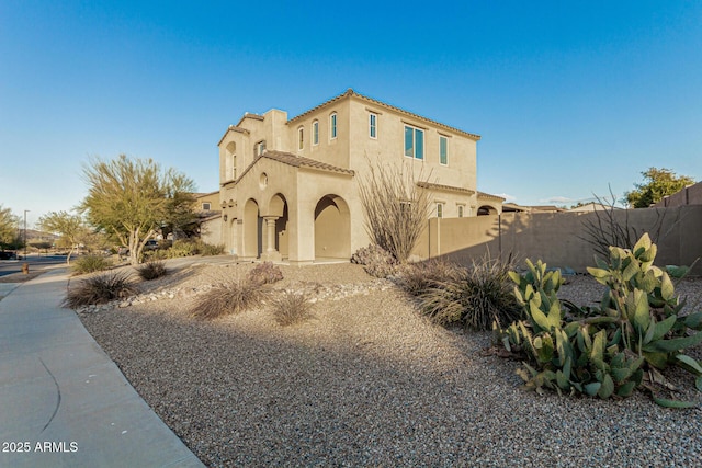mediterranean / spanish-style home featuring a tiled roof, stucco siding, and fence