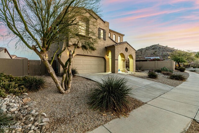 mediterranean / spanish-style home featuring fence, a tiled roof, an attached garage, stucco siding, and driveway
