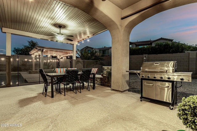 patio terrace at dusk with a fenced backyard, outdoor dining space, a grill, and a ceiling fan