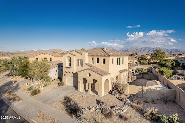 mediterranean / spanish-style home featuring driveway, an attached garage, a fenced backyard, stucco siding, and a mountain view