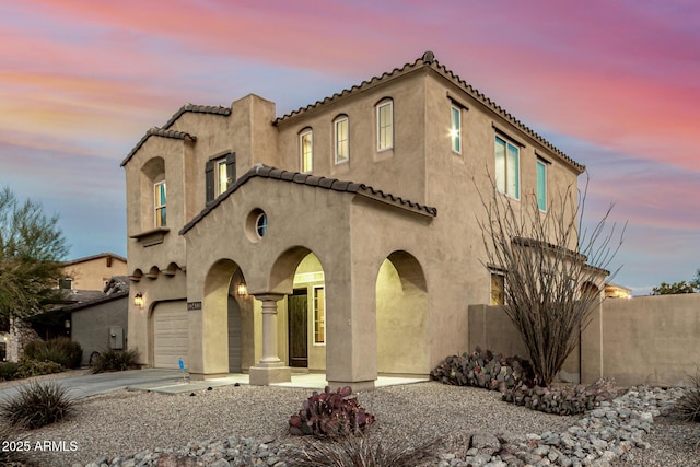 mediterranean / spanish-style home featuring a tiled roof, stucco siding, an attached garage, and concrete driveway