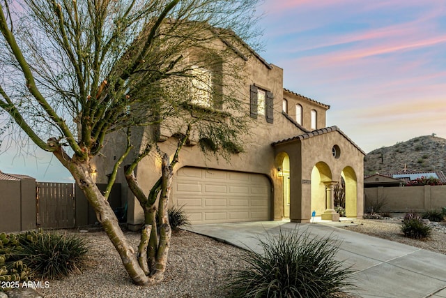 view of front of property with fence, a tiled roof, a garage, stucco siding, and driveway