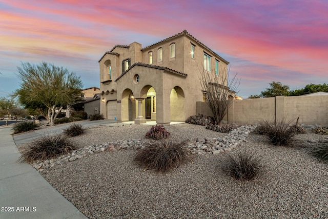 mediterranean / spanish house featuring a tile roof, concrete driveway, stucco siding, and fence