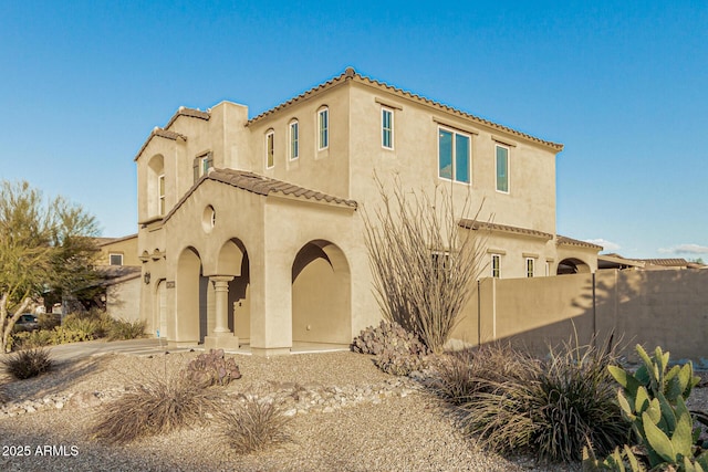 mediterranean / spanish home with a tiled roof, stucco siding, and fence