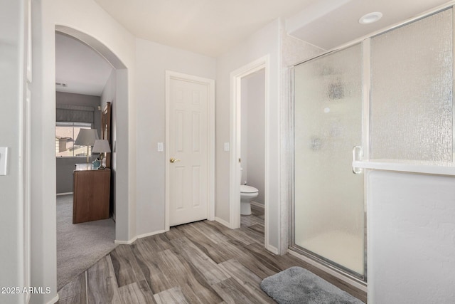 bathroom featuring hardwood / wood-style flooring, a shower with door, and toilet