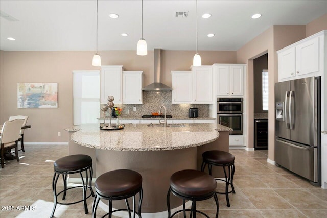 kitchen featuring white cabinets, appliances with stainless steel finishes, decorative light fixtures, and wall chimney range hood