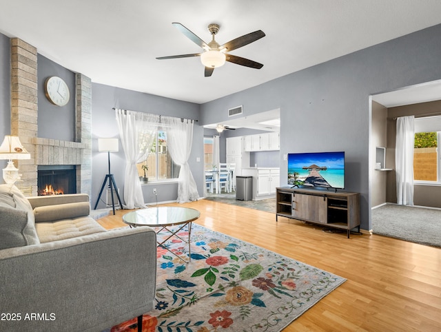 7726 W Cameron Dr, Peoria, AZ 85345 - living room with ceiling fan, a fireplace, visible vents, light wood finished floors, and baseboards