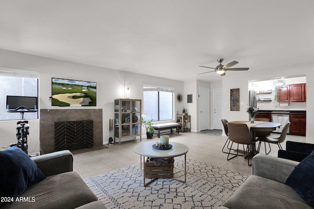 living room with ceiling fan, a tile fireplace, and light tile patterned floors