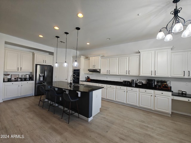 kitchen featuring fridge with ice dispenser, a center island with sink, a kitchen breakfast bar, light hardwood / wood-style flooring, and decorative light fixtures