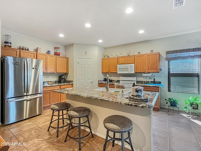 kitchen with a center island with sink, a breakfast bar, light stone countertops, sink, and white appliances