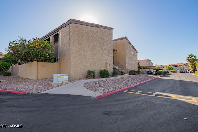 view of side of property with stairway, uncovered parking, stucco siding, and a tile roof