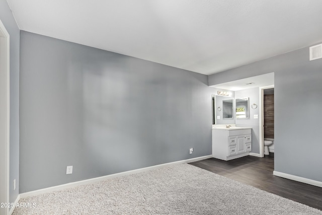 unfurnished bedroom with baseboards, dark colored carpet, connected bathroom, a sink, and dark wood finished floors